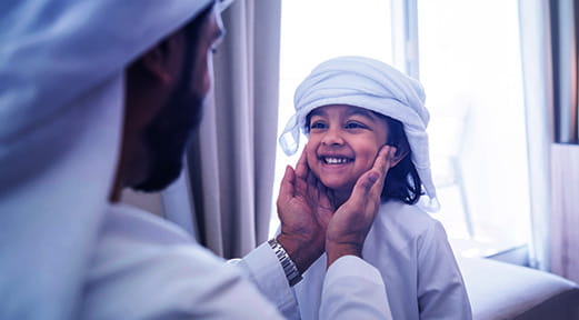 A man holds his child's face, reflecting the security and stability that can be achieved by refinancing a mortgage with First Abu Dhabi Islamic Bank.